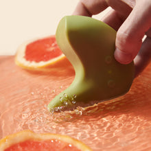 Load image into Gallery viewer, Photo of the boomerang shaped Kiwi pelvic vibrator vibrating in a shallow pool of water with slices of grapefruit around it
