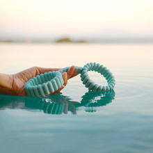Load image into Gallery viewer, Lifestyle photo of a woman's hand holding out the Biird silicone handcuffs over a calm pool of water.