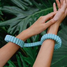 Load image into Gallery viewer, Lifestyle photo of a woman's hands and wrists wearing the Biird Silicone Handcuffs in front of giant tropical leaves.