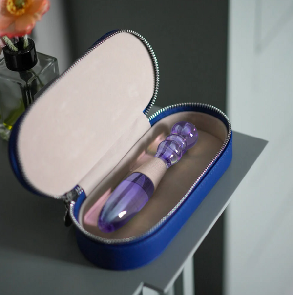 Biird Cecii Luxury Glass Dildo in purple and clear glass. Shown in its open case on a nightstand next to flowers.