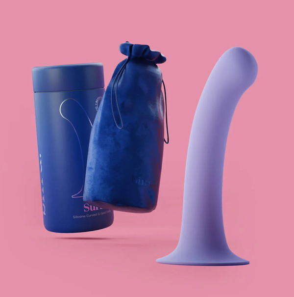 Biird Surii Silicone Suction Cup Dildo shown in lilac on a pink background, alongside navy blue bag & container. 