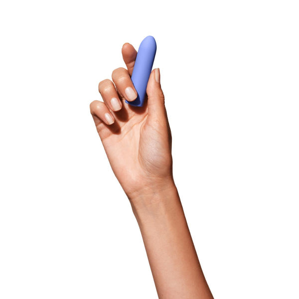 Hand holding up a Dame Zee rechargeable bullet vibrator in periwinkle against a white background