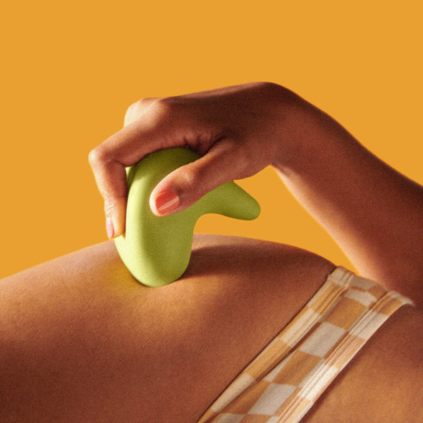 Photo of the Kiwi vibrator by The Pelvic People. A woman in a checked bikini holds the boomerang shaped vibrator against her hip in front of an orange background
