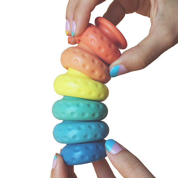 White background with hands holding siz different Ohnut intimacy bumpers in the colours of the rainbow