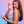 Smiling female model in lilac top holding up the VUSH Plump Rechargeable Palm Vibrator in light pink alongside its cap and case.