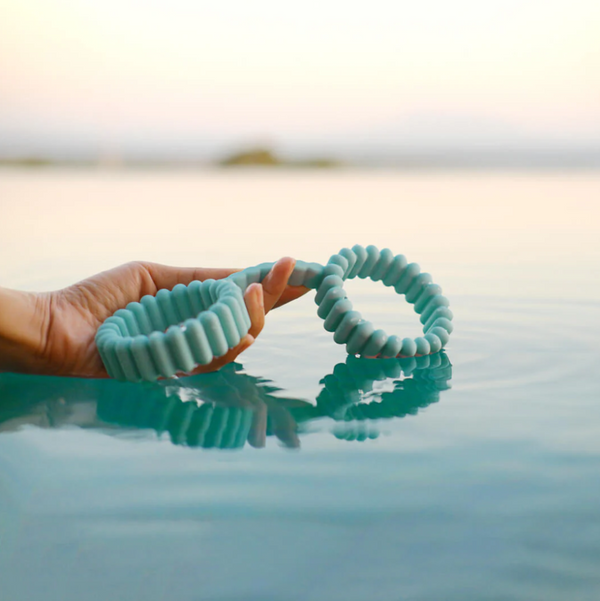 Lifestyle photo of a woman's hand holding out the Biird silicone handcuffs over a calm pool of water.