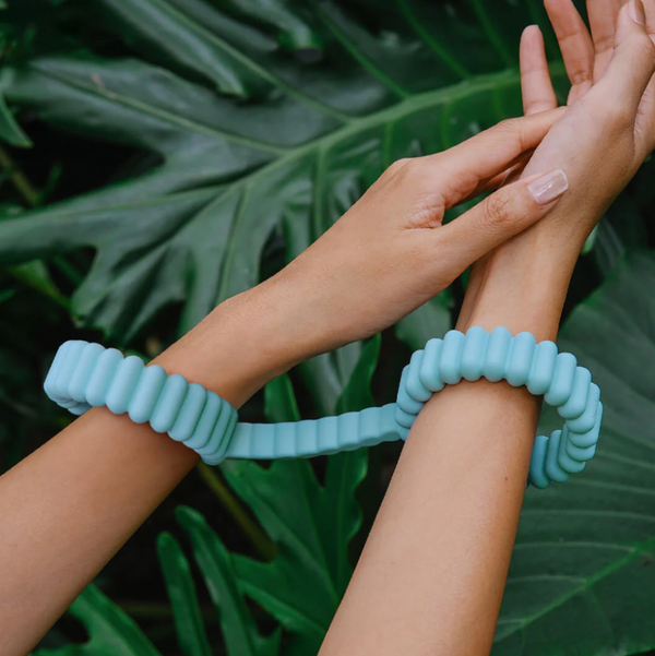 Lifestyle photo of a woman's hands and wrists wearing the Biird Silicone Handcuffs in front of giant tropical leaves.