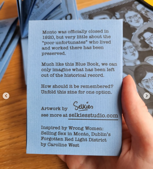 Hand holding a rear view of the blue education zine about Monto, by the artist Selkies. Over a brown table background and other zines.