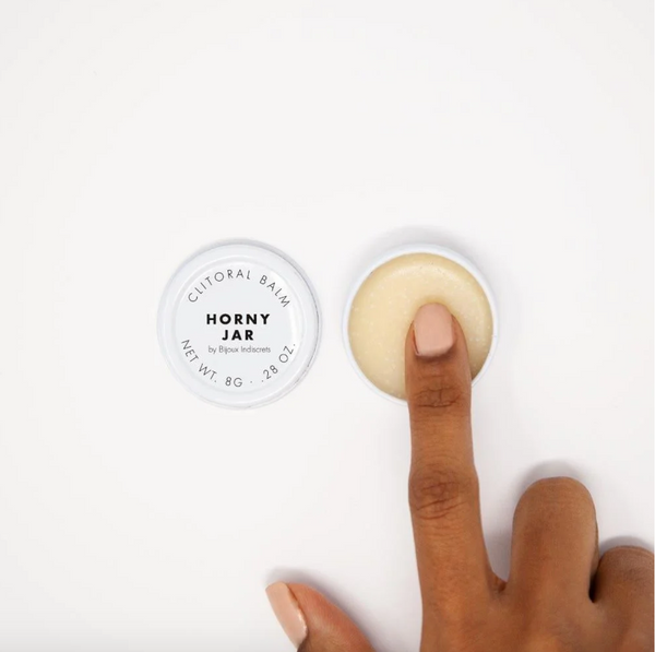 Open jar of Bijou Indiscreets Horny Jar Clitoral Balm alongside the lid, with finger swiping some of the contents