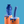 A single Biird Boo & Bae Silicone Suction Cup Dildo in grainy blue and white. Shown Stood on a dripping orange pillar on a blue background. Alongside a Biird bag and fingering keychain on an orange dripping pillar.