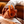 Two people holding hands outstretched on a couch with one of them holding the Vush Orb cock ring in Orange.
