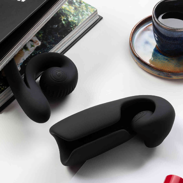 Lifestyle photograph of the Evo rechargeable and extendable penis vibrator from Snail Vibe on a table next to a book and cup of coffee. 