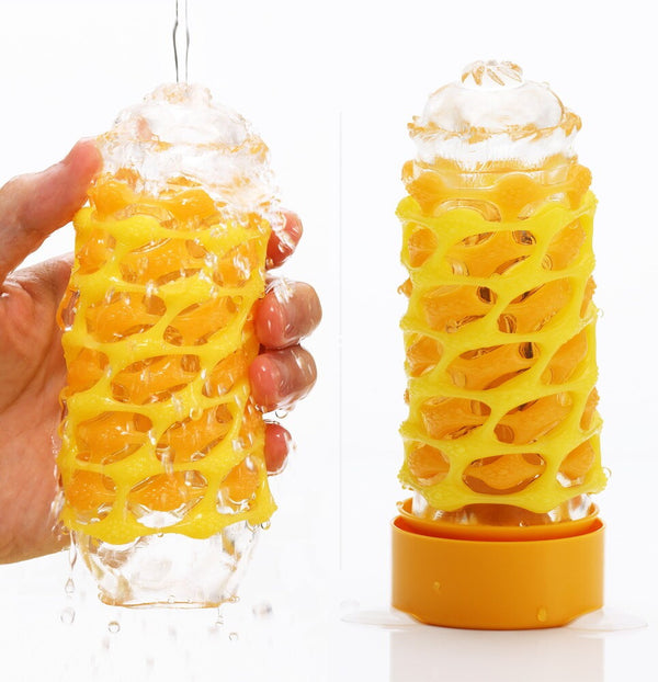 Side view of two Tenga Arte Weave out of their packaging, yellow/orange theme. One is being held by a hand with lubrication, the other is on its stand.