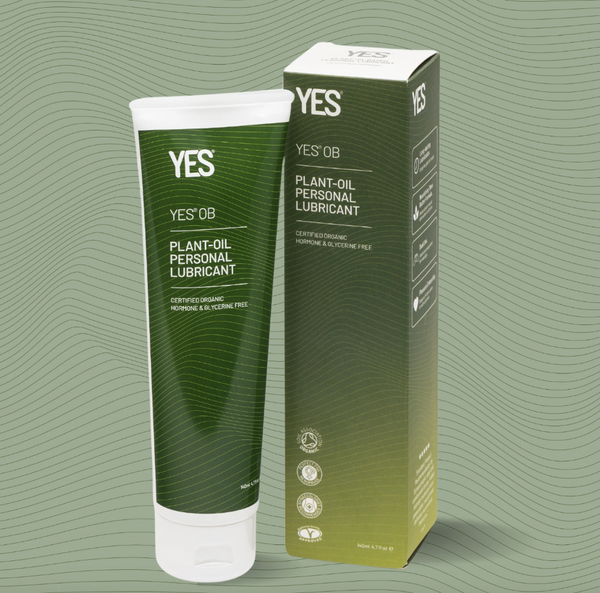 A 140ml bottle of Yes OB plant oil based lubricant next to an example of its green cardboard packaging, on a light green wavy background.