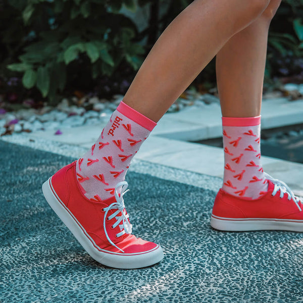 Biird branded Clit Socks in a pink and light pink colour scheme being worn on bare legs in red shoes in a walking outdoor scenario