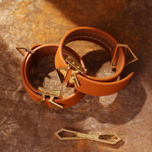 Load image into Gallery viewer, Top down view of LOCKINK Leather Cuffs laid on top of one another with a rustic straw coloured background. Alongside a LOCKINK buckle.