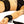 Close up on the wrist of a female model lying on white bed sheets being restrained by the Sei Mio Bed-Spreader Under Bed Restraint System in black.