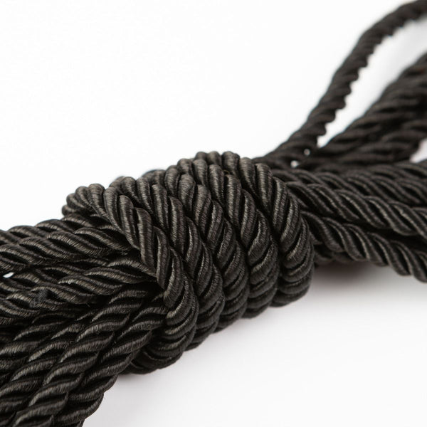 Close up of the texture of a wrapped up SEI MIO - Knot in Control - 10m Silky Bondage Rope in black on a white background.