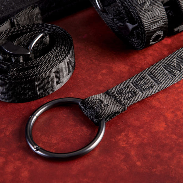 Close up of the strap and buckle components. Part of the Sei Mio Bed-Spreader Under Bed Restraint System in black, on a red background.