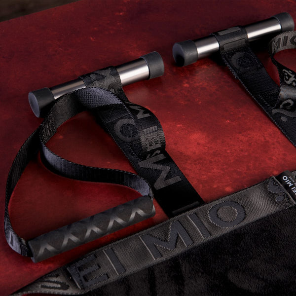Close up of the strap and bar components of the SEI MIO - Behind Closed Doors - Adjustable Door Hanging Sex Swing in black on a red crushed velvet background