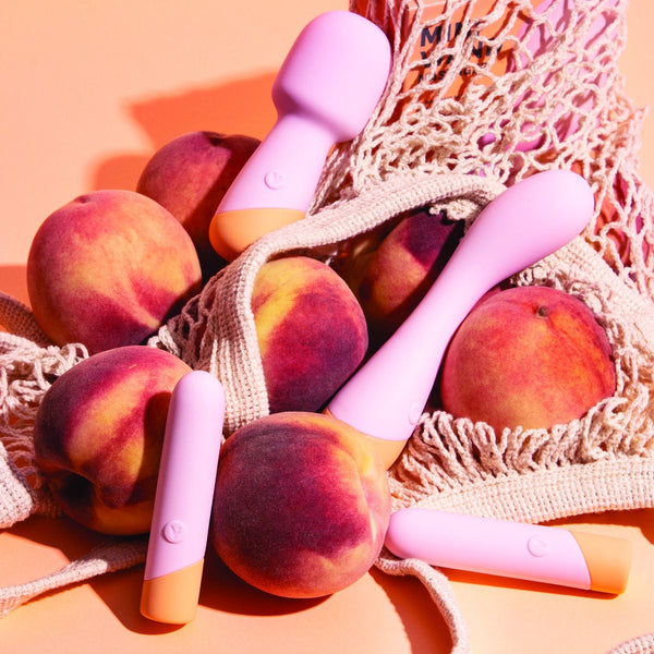 Lifestyle photo of various Vush Peachy Mini Wands laid out on a net bag filled with actual peaches. 