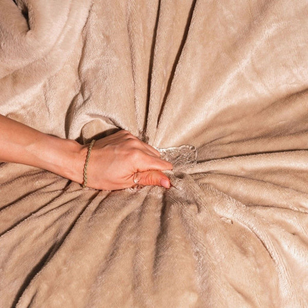 Image shows a woman's hand squeezing water into a cream coloured faux fur splash blanket to demonstrate that it is waterproof. 