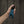 Mood photo of a hand holding a turquoise Fun Factory Manta blow job vibrator for couples. Toy has a black handle, and background is of a fence - Sex Siopa, Ireland's favourite sex toy shop