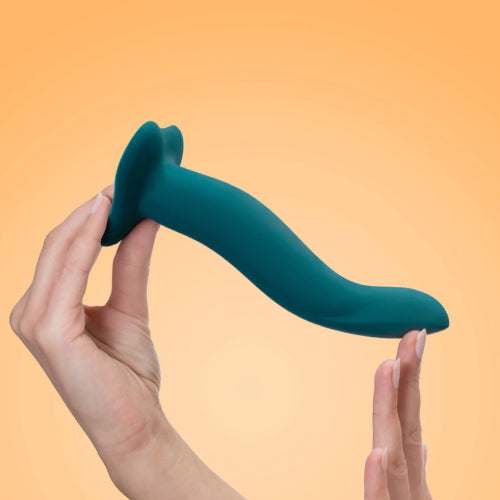 Picture of female hands holding the Fun Factory Limba Flex silicone dildo with suction base for a strap-on harness. Coloured in dark green this is set on a light orange background. The Limba Flex comes in a small and medium size. Available at SexSiopa.ie, Ireland's favourite sex toy retailer.