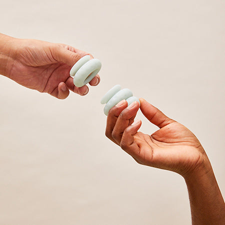 Picture of hands holding some Ohnut intimacy bumpers in white. The Ohnut is a stackable wearable cock ring to help with pain during intercourse. It is silicone and can be used for folks who suffer from vaginismus, endometriosis, or who have had a hysterectomy.