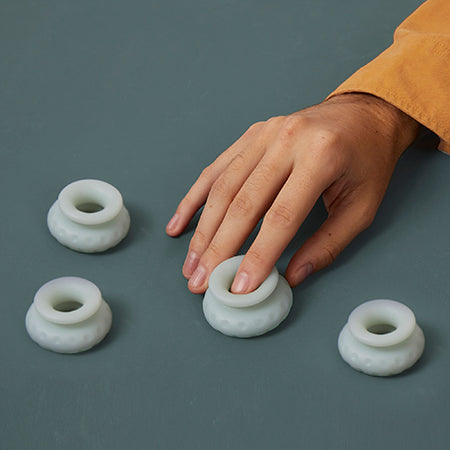 Picture of a hand with a yellow sleeve playing with some white unstacked Ohnut silicone intimacy bumpers. Scene set on a grey background. The Ohnut tool is for more comfortable sex for people who have endometriosis - Sex Siopa Ireland