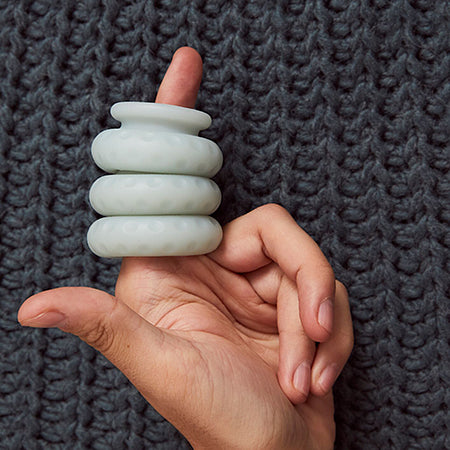 Hand with finger holding a stack of Ohnut silicone bumpers that help prevent pain during sex for people with endometriosis. Shown on a textured fabric background - Sex Siopa Ireland